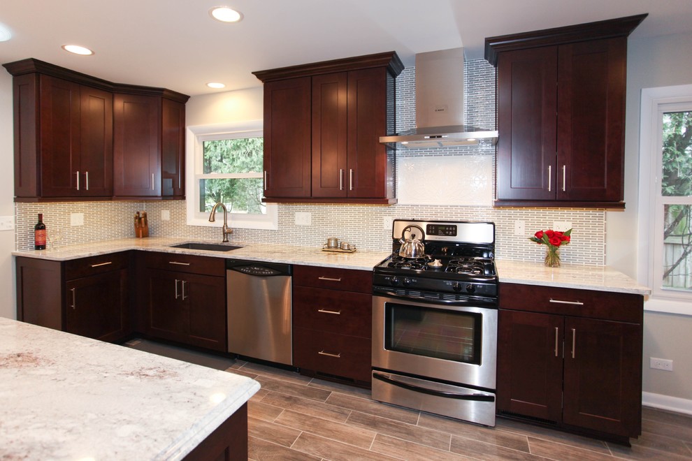 Eat-in kitchen - large transitional u-shaped porcelain tile eat-in kitchen idea in Chicago with an undermount sink, recessed-panel cabinets, dark wood cabinets, granite countertops, gray backsplash, glass tile backsplash, stainless steel appliances and an island