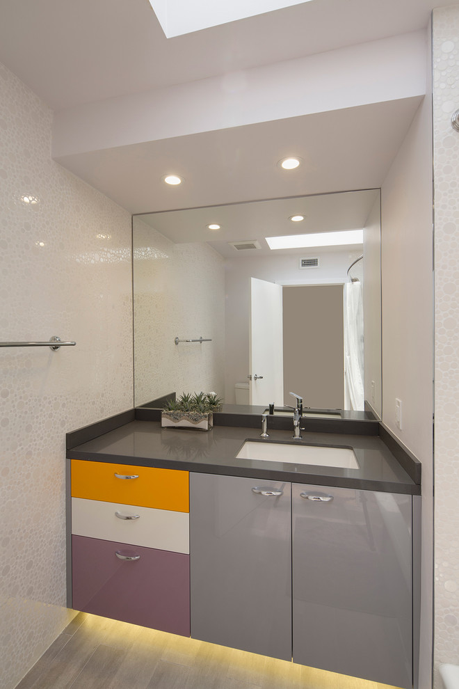 Photo of a contemporary 3/4 bathroom in Los Angeles with an undermount sink, flat-panel cabinets, grey cabinets, a shower/bathtub combo, white tile, mosaic tile, white walls, limestone benchtops and light hardwood floors.
