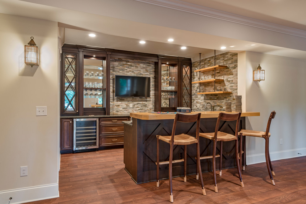 Large transitional u-shaped seated home bar in Raleigh with an undermount sink, beaded inset cabinets, dark wood cabinets, granite benchtops, grey splashback, stone tile splashback, vinyl floors and brown floor.