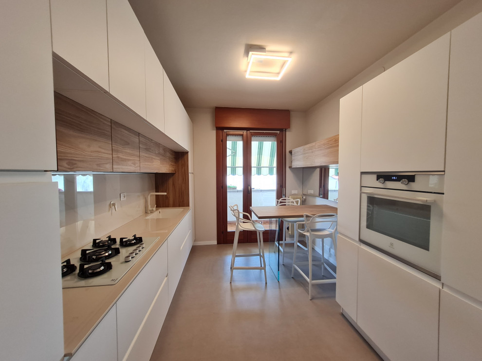 Photo of a mid-sized contemporary galley separate kitchen in Other with an undermount sink, white cabinets, marble benchtops, white appliances, vinyl floors and beige floor.