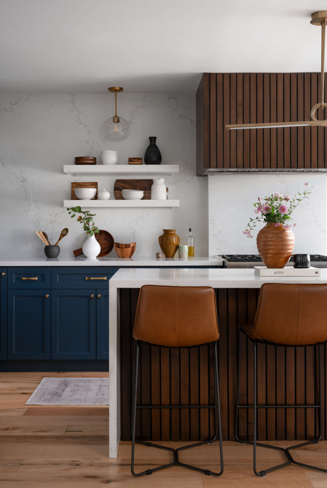 Example of a mid-sized transitional l-shaped medium tone wood floor and beige floor eat-in kitchen design in Toronto with a farmhouse sink, shaker cabinets, blue cabinets, quartz countertops, white backsplash, quartz backsplash, stainless steel appliances, an island and white countertops