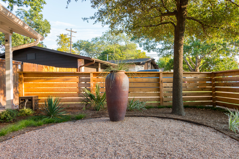 Photo of a mid-sized and desert look contemporary front yard partial sun xeriscape for summer in Austin with a wood fence and gravel.