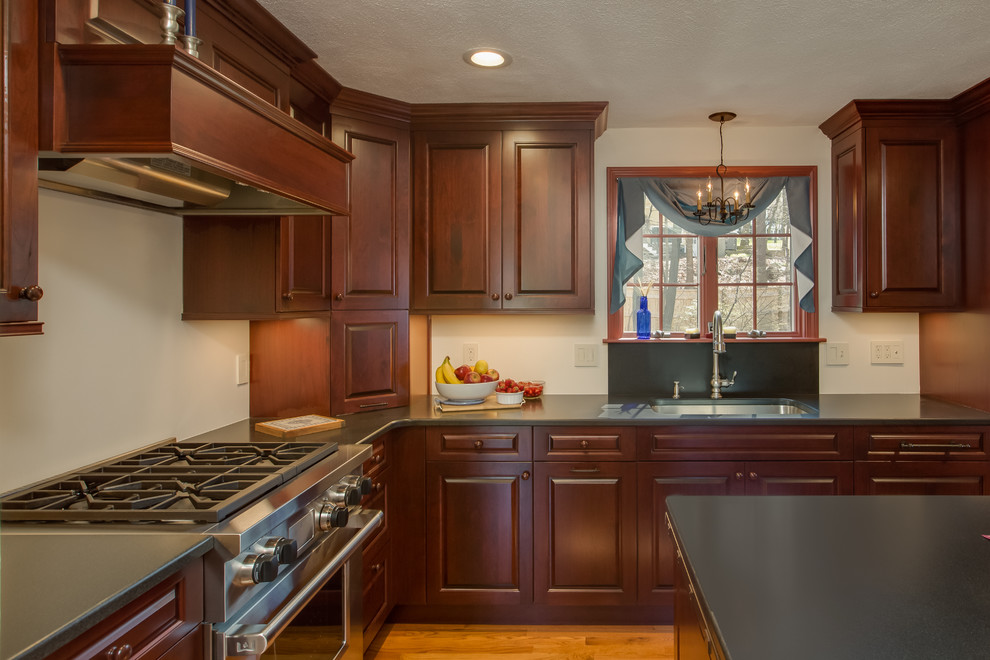 Traditional l-shaped eat-in kitchen in Boston with a drop-in sink, raised-panel cabinets, dark wood cabinets, solid surface benchtops, medium hardwood floors and with island.