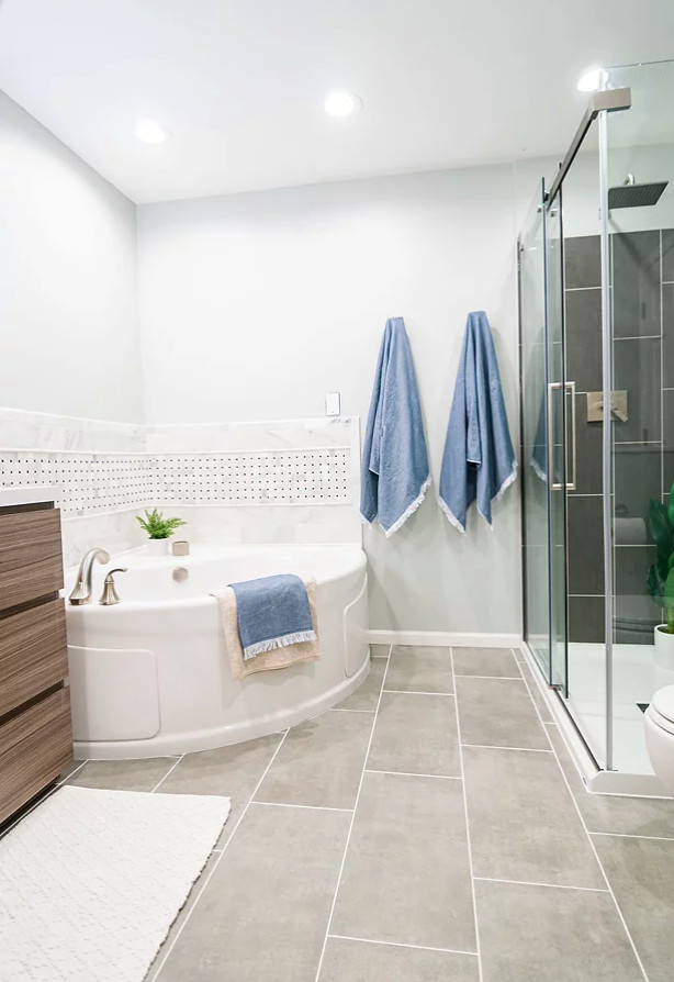 Photo of a mid-sized transitional master bathroom in Minneapolis with flat-panel cabinets, medium wood cabinets, a corner tub, a corner shower, a one-piece toilet, gray tile, grey walls, ceramic floors, an undermount sink, engineered quartz benchtops, grey floor, a sliding shower screen, white benchtops, a double vanity and a freestanding vanity.