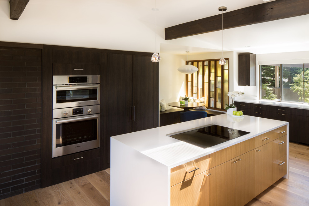 Photo of a large contemporary u-shaped eat-in kitchen in Seattle with a single-bowl sink, flat-panel cabinets, dark wood cabinets, quartz benchtops, white splashback, stone slab splashback, stainless steel appliances, light hardwood floors and with island.