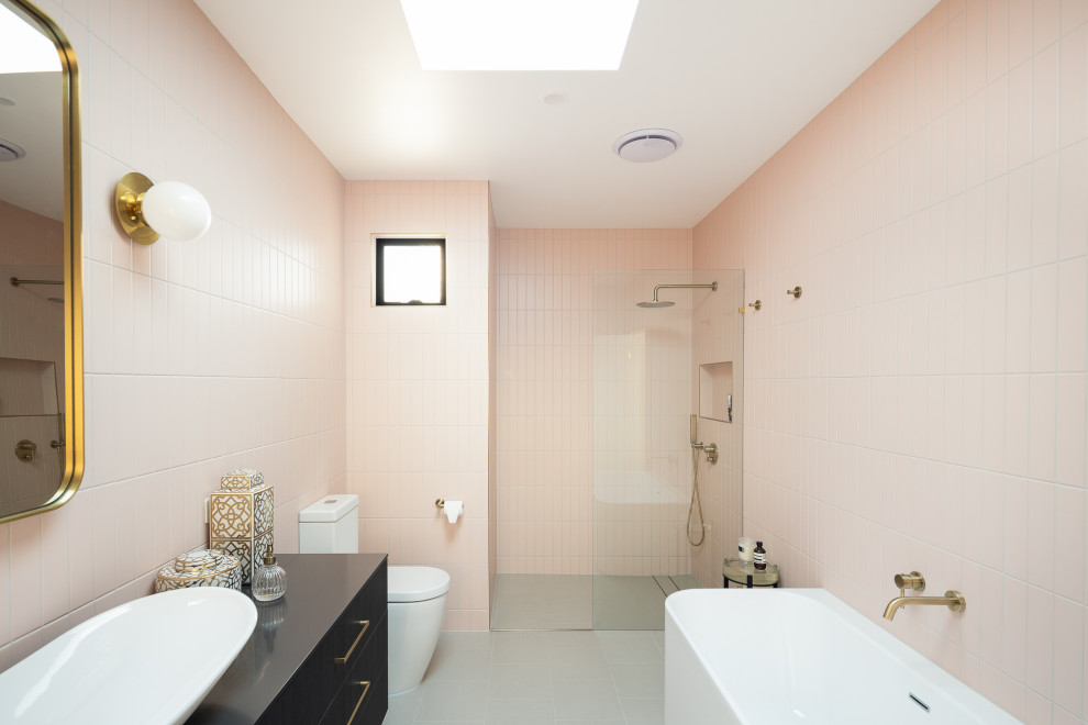 На фото: ванная комната среднего размера в стиле модернизм с фасадами островного типа, темными деревянными фасадами, отдельно стоящей ванной, открытым душем, унитазом-моноблоком, розовой плиткой, удлиненной плиткой, розовыми стенами, полом из керамической плитки, душевой кабиной, настольной раковиной, столешницей из ламината, серым полом, открытым душем, черной столешницей, тумбой под одну раковину и подвесной тумбой с