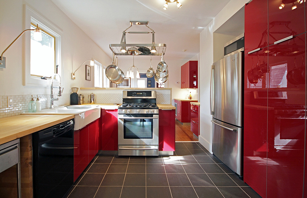 Photo of a large country galley separate kitchen in Houston with stainless steel appliances, wood benchtops, red cabinets, a farmhouse sink, flat-panel cabinets, white splashback, ceramic splashback, slate floors, a peninsula and black floor.