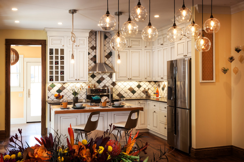 Inspiration for a mid-sized transitional l-shaped medium tone wood floor and brown floor eat-in kitchen remodel in Denver with a farmhouse sink, raised-panel cabinets, multicolored backsplash, ceramic backsplash, stainless steel appliances, an island, white cabinets and solid surface countertops