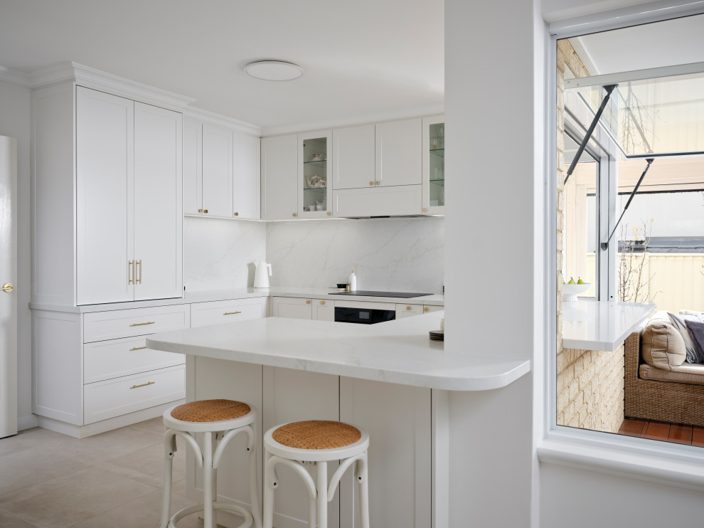 Design ideas for a transitional u-shaped kitchen in Perth with shaker cabinets, white cabinets, white splashback, stone slab splashback, black appliances, a peninsula, grey floor and white benchtop.