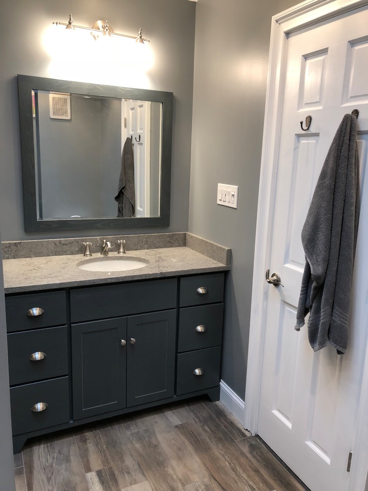 This is an example of a mid-sized country master bathroom in New York with dark wood cabinets, an alcove tub, a corner shower, a one-piece toilet, gray tile, ceramic tile, grey walls, ceramic floors, an undermount sink, granite benchtops, grey floor and a sliding shower screen.
