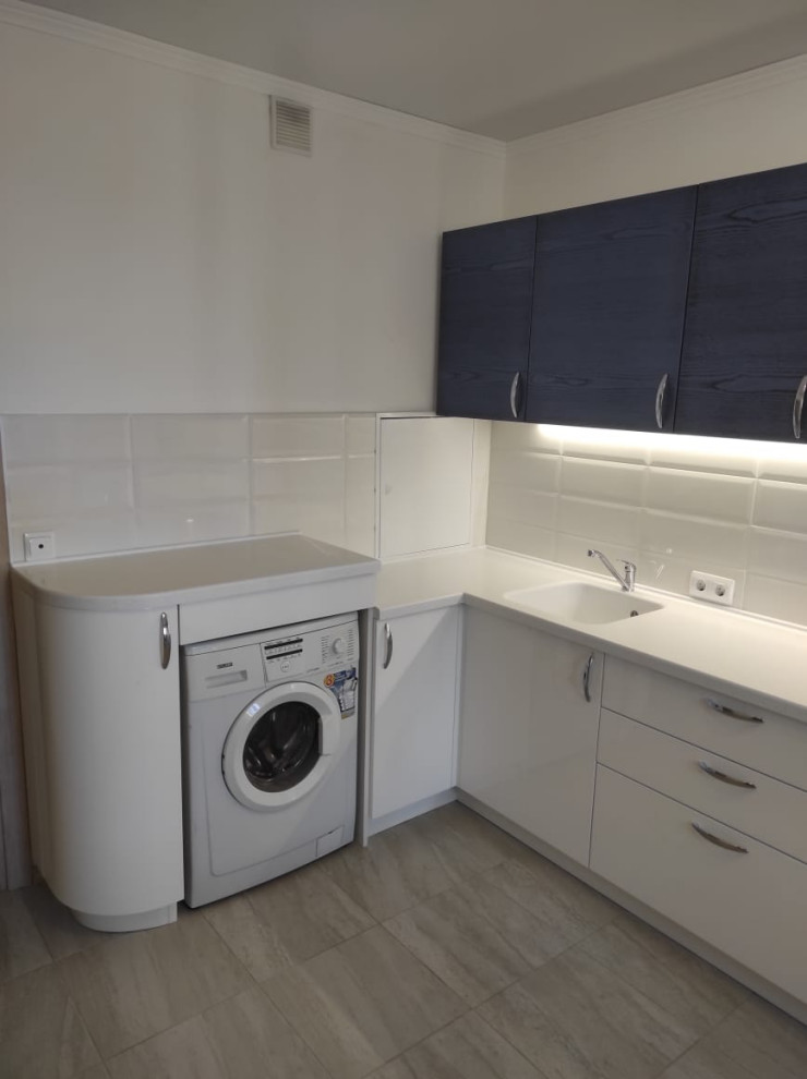 This is an example of a mid-sized contemporary l-shaped eat-in kitchen in Moscow with an undermount sink, flat-panel cabinets, blue cabinets, white splashback, ceramic splashback, white appliances, ceramic floors, no island, beige floor and white benchtop.