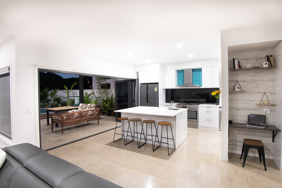 Photo of a beach style kitchen with white cabinets, quartz benchtops, stainless steel appliances, concrete floors, with island and white benchtop.