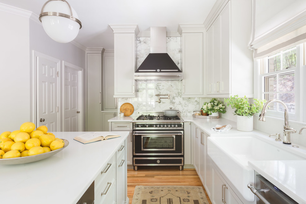 Inspiration for a traditional l-shaped kitchen in Other with a farmhouse sink, recessed-panel cabinets, white cabinets, white splashback, stone slab splashback, black appliances, medium hardwood floors, with island, brown floor and white benchtop.