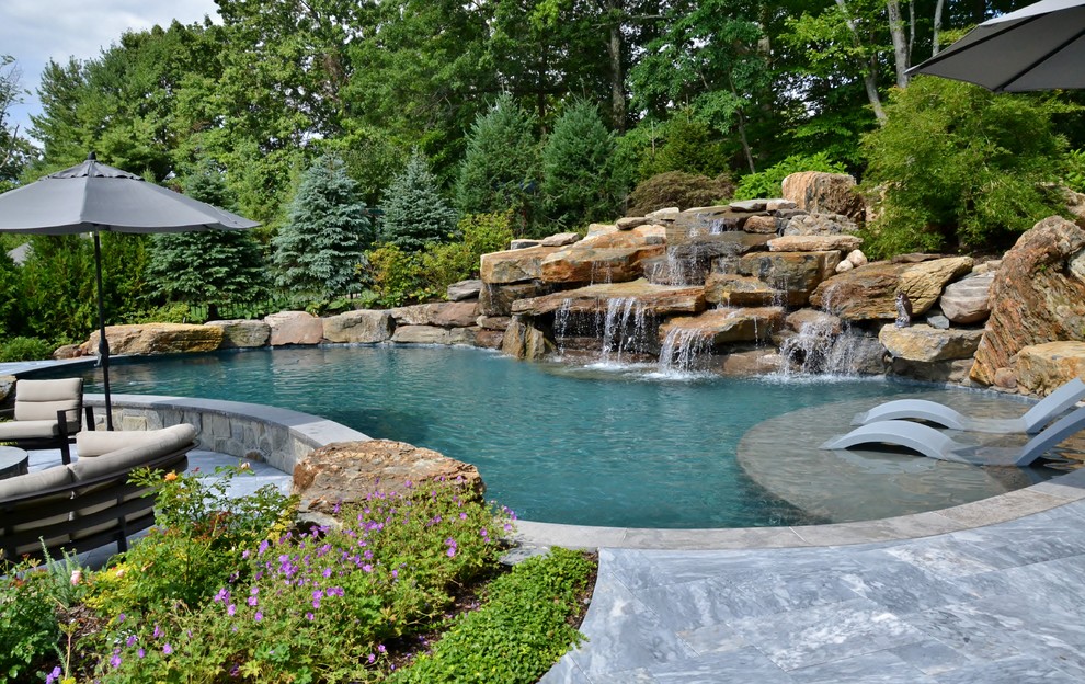 This is an example of a large country backyard kidney-shaped natural pool in New York with natural stone pavers.