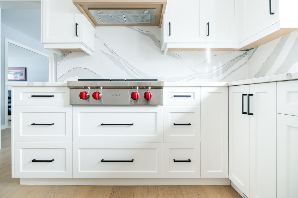 Inspiration for a mid-sized transitional u-shaped light wood floor eat-in kitchen remodel in Toronto with an undermount sink, shaker cabinets, white cabinets, quartz countertops, white backsplash, quartz backsplash, stainless steel appliances, an island and white countertops