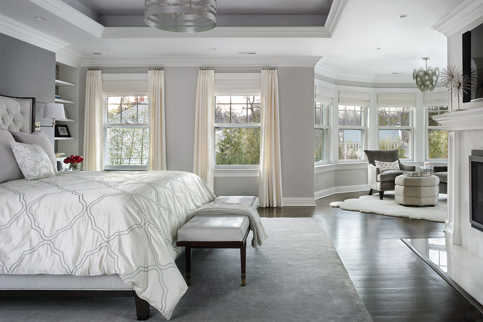 Large traditional master bedroom in New York with grey walls, dark hardwood floors, a standard fireplace, a stone fireplace surround and brown floor.