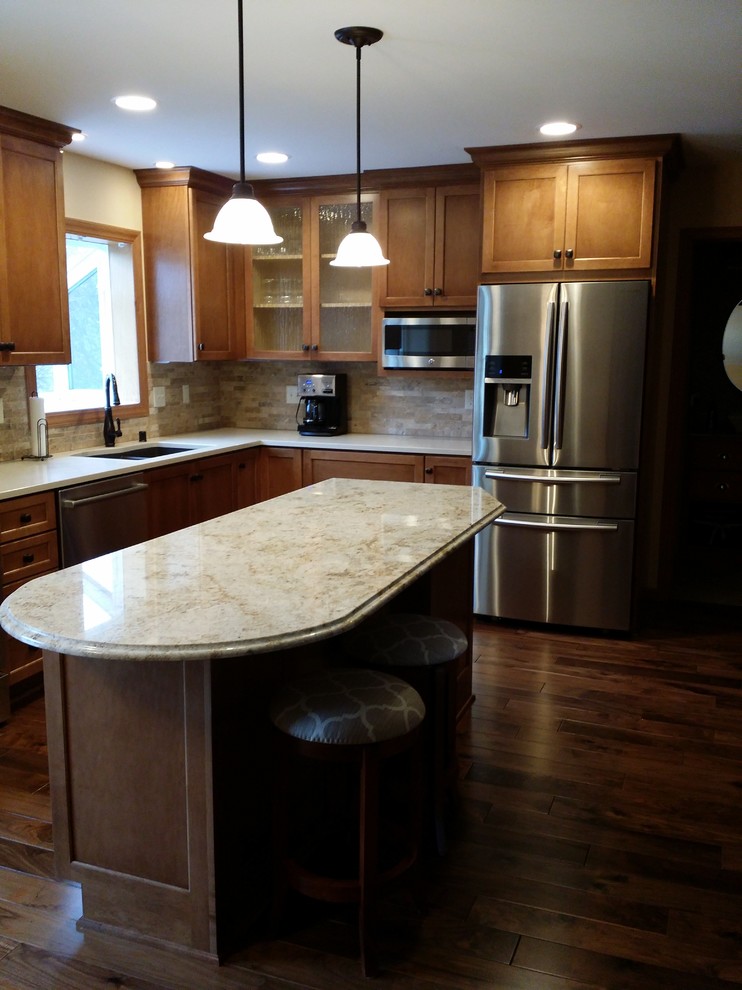 Inspiration for a mid-sized transitional l-shaped medium tone wood floor eat-in kitchen remodel in Milwaukee with an undermount sink, shaker cabinets, medium tone wood cabinets, granite countertops, beige backsplash, stone tile backsplash, stainless steel appliances and an island