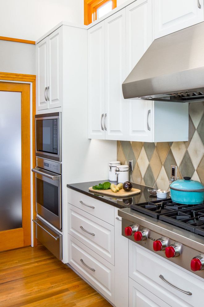 Example of a mid-sized transitional u-shaped medium tone wood floor enclosed kitchen design in Austin with an undermount sink, raised-panel cabinets, white cabinets, granite countertops, green backsplash, ceramic backsplash, stainless steel appliances and an island