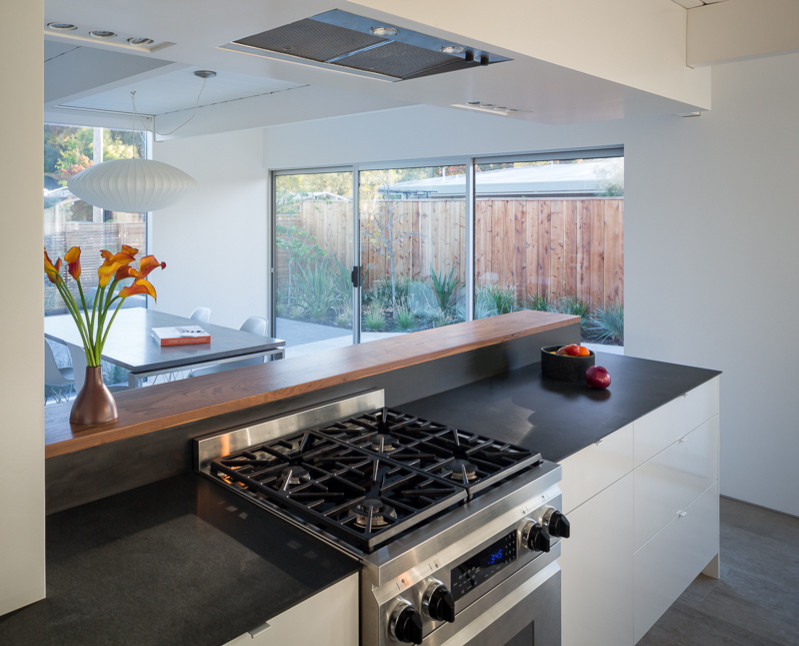 This is an example of a mid-sized midcentury galley eat-in kitchen in San Francisco with an undermount sink, flat-panel cabinets, white cabinets, white splashback, glass sheet splashback, stainless steel appliances, solid surface benchtops, porcelain floors, beige floor and exposed beam.