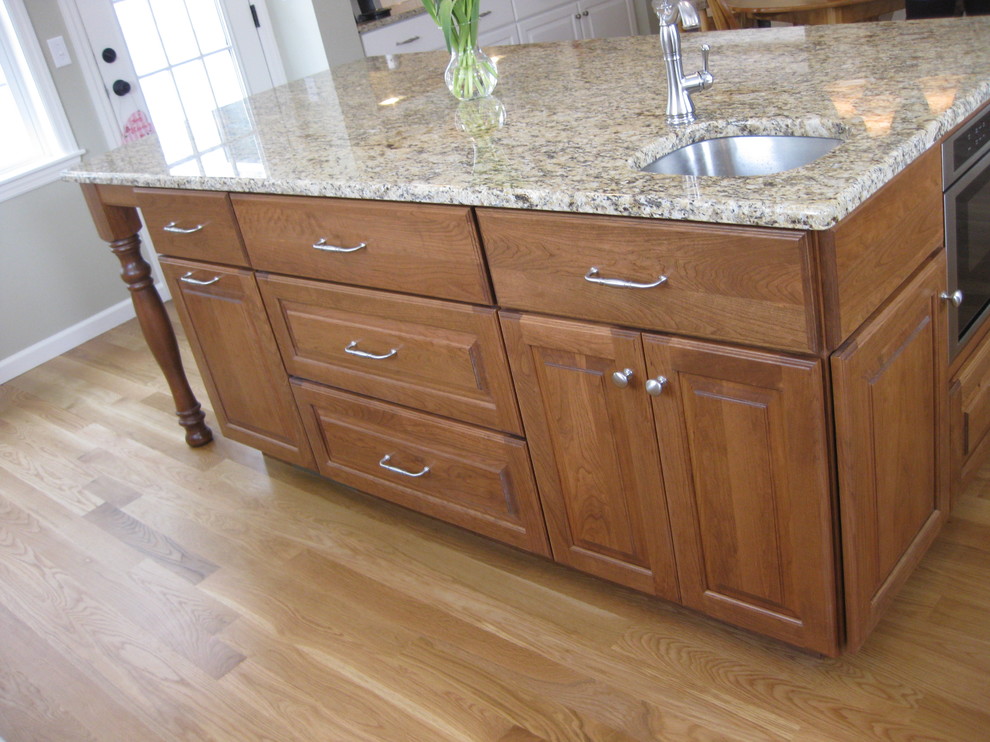 Transitional u-shaped medium tone wood floor eat-in kitchen photo in Boston with an undermount sink, raised-panel cabinets, white cabinets, granite countertops, white backsplash, ceramic backsplash, stainless steel appliances, an island and beige countertops