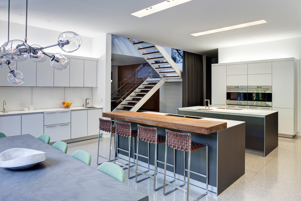 Photo of an industrial eat-in kitchen in Chicago with flat-panel cabinets, white cabinets, stainless steel appliances and wood benchtops.