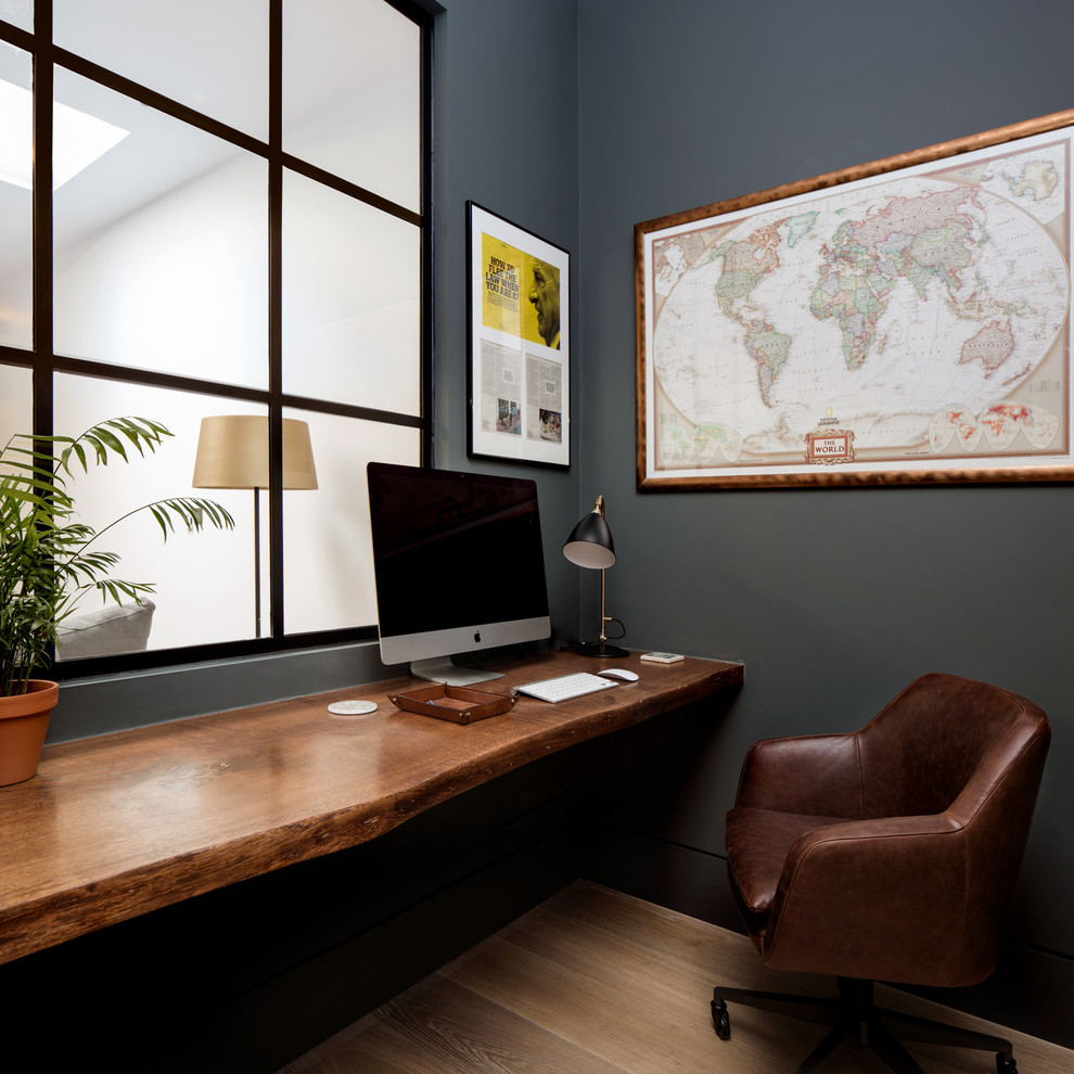 Photo of a small contemporary study room in London with black walls, light hardwood floors, a built-in desk and beige floor.