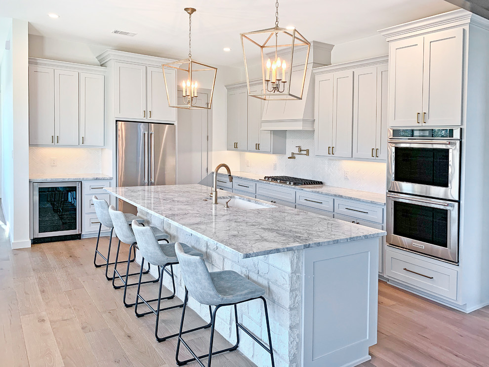 Inspiration for a transitional l-shaped light wood floor and beige floor kitchen remodel in Austin with an undermount sink, shaker cabinets, white cabinets, white backsplash, stainless steel appliances, an island and gray countertops