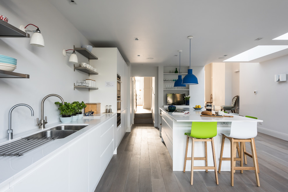 Inspiration for a large contemporary open plan kitchen in London with flat-panel cabinets, white cabinets, stainless steel appliances, light hardwood floors, with island and a double-bowl sink.