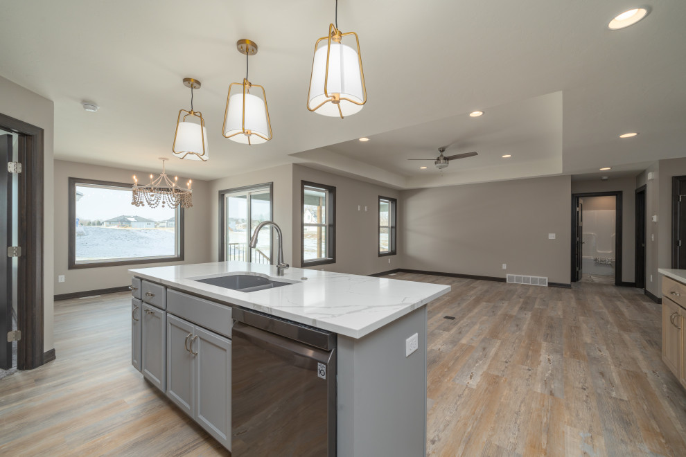 Example of a transitional l-shaped vinyl floor and multicolored floor open concept kitchen design with an undermount sink, shaker cabinets, light wood cabinets, quartz countertops, beige backsplash, black appliances, an island and white countertops