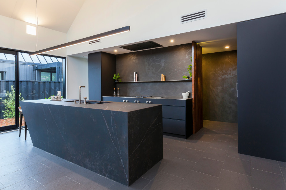 Inspiration for a mid-sized contemporary galley eat-in kitchen in Christchurch with with island, an undermount sink, flat-panel cabinets, black cabinets, black splashback, porcelain splashback, stainless steel appliances, porcelain floors and black floor.