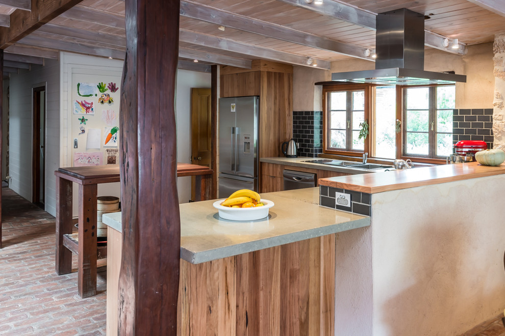 Inspiration for a mid-sized country l-shaped eat-in kitchen in Adelaide with a double-bowl sink, flat-panel cabinets, medium wood cabinets, concrete benchtops, black splashback, subway tile splashback, stainless steel appliances, brick floors and with island.
