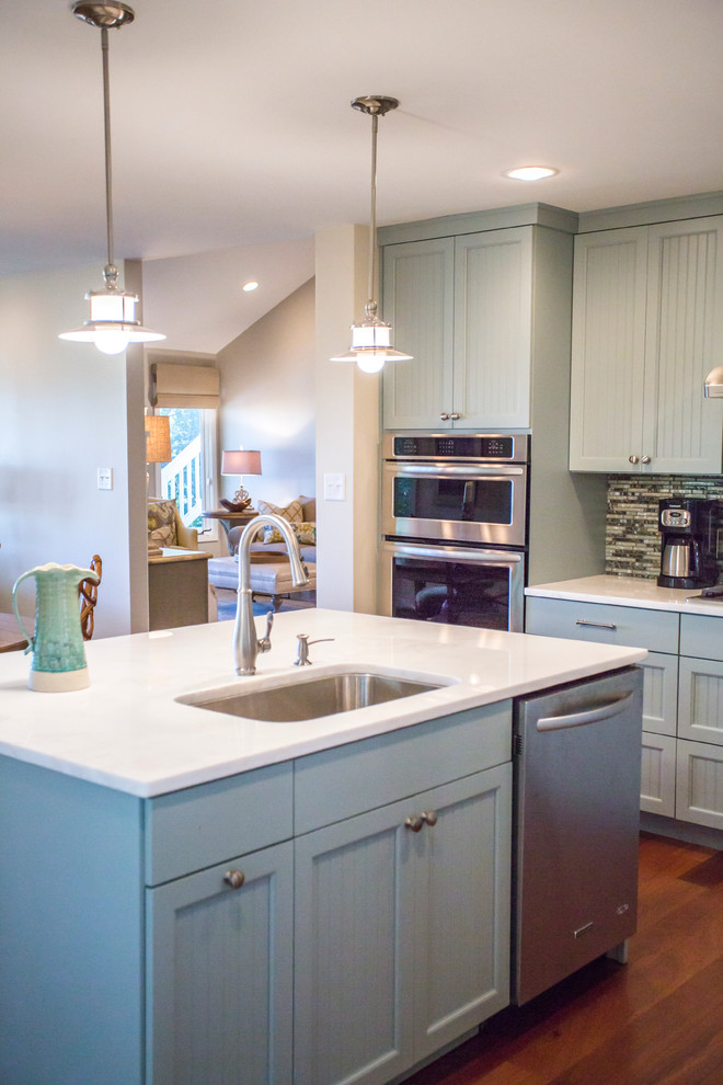 This is an example of a mid-sized beach style l-shaped eat-in kitchen in Atlanta with an undermount sink, louvered cabinets, blue cabinets, blue splashback, glass tile splashback, stainless steel appliances, medium hardwood floors and with island.