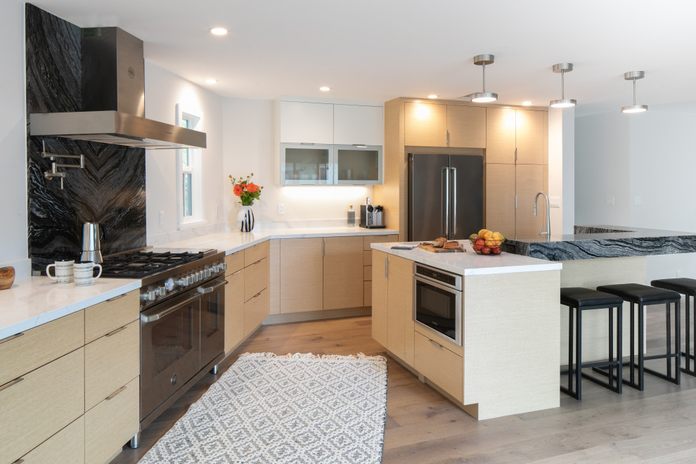 Photo of a large contemporary l-shaped eat-in kitchen in San Francisco with flat-panel cabinets, light wood cabinets, quartz benchtops, stone slab splashback, stainless steel appliances, light hardwood floors, with island, white benchtop, black splashback and beige floor.