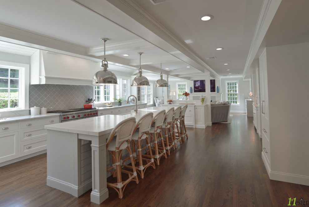 Open concept kitchen - mid-sized transitional u-shaped medium tone wood floor and brown floor open concept kitchen idea in Boston with a farmhouse sink, recessed-panel cabinets, white cabinets, quartzite countertops, gray backsplash, glass tile backsplash, paneled appliances, an island and white countertops