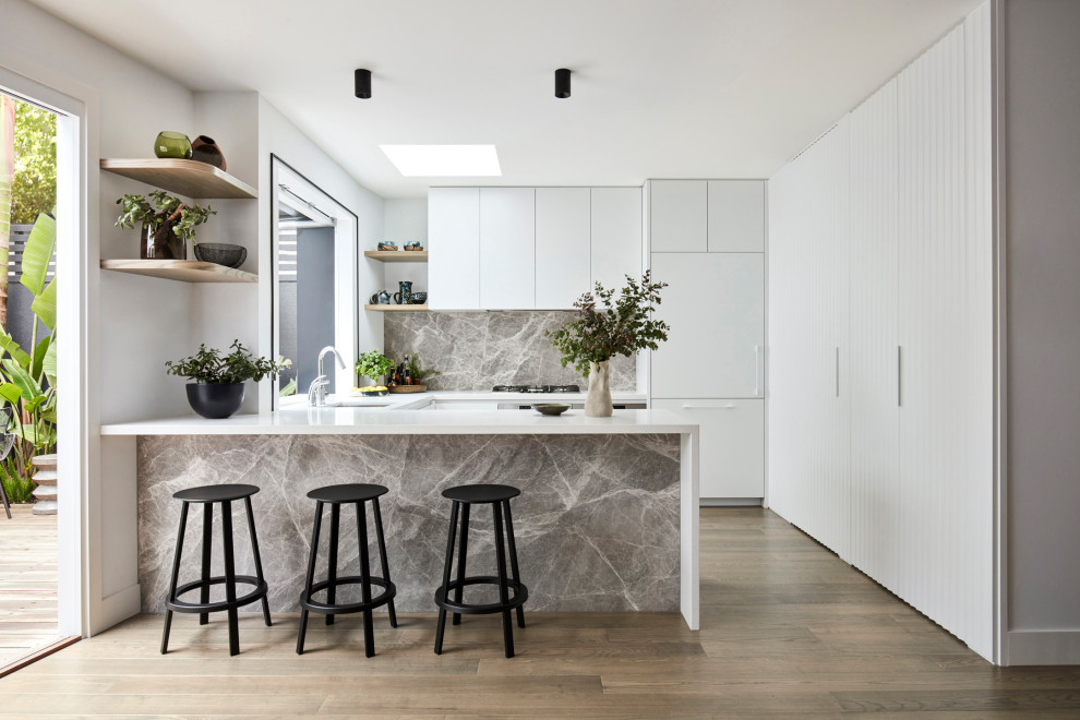 Inspiration for a mid-sized contemporary u-shaped kitchen in Melbourne with an undermount sink, flat-panel cabinets, white cabinets, quartz benchtops, grey splashback, stone slab splashback, medium hardwood floors, a peninsula, brown floor, white benchtop and panelled appliances.