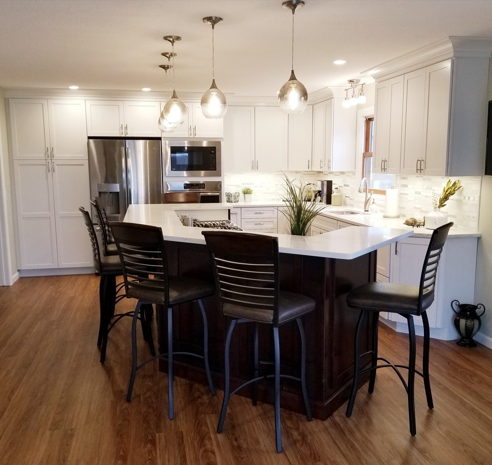 Large transitional l-shaped medium tone wood floor and brown floor open concept kitchen photo in Chicago with a double-bowl sink, shaker cabinets, white cabinets, quartzite countertops, white backsplash, stainless steel appliances and an island
