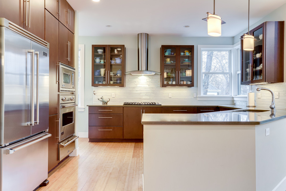Contemporary u-shaped eat-in kitchen in DC Metro with an undermount sink, glass-front cabinets, medium wood cabinets, quartz benchtops, white splashback, matchstick tile splashback, stainless steel appliances, medium hardwood floors, a peninsula, brown floor and brown benchtop.