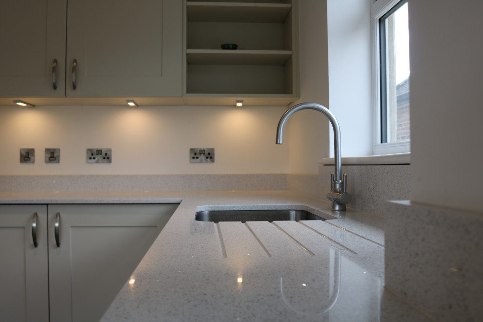 Photo of a mid-sized traditional l-shaped eat-in kitchen in Sussex with an undermount sink, shaker cabinets, beige cabinets, quartzite benchtops, white splashback, cement tile splashback, black appliances, porcelain floors, with island, beige floor and white benchtop.