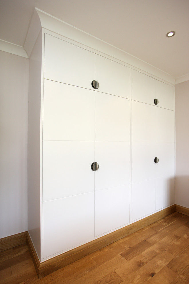 Photo of a large modern gender-neutral built-in wardrobe in London with medium hardwood floors, brown floor, flat-panel cabinets and white cabinets.
