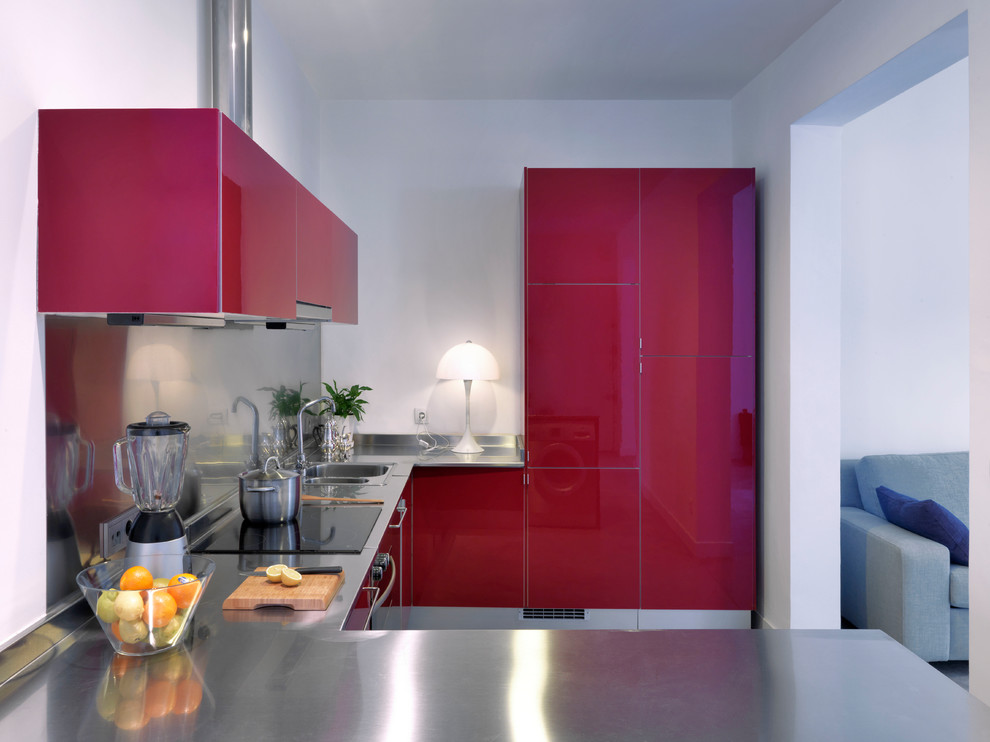 Small contemporary u-shaped open plan kitchen in Madrid with an integrated sink, flat-panel cabinets, red cabinets, stainless steel benchtops, metallic splashback, metal splashback, stainless steel appliances, a peninsula and grey floor.