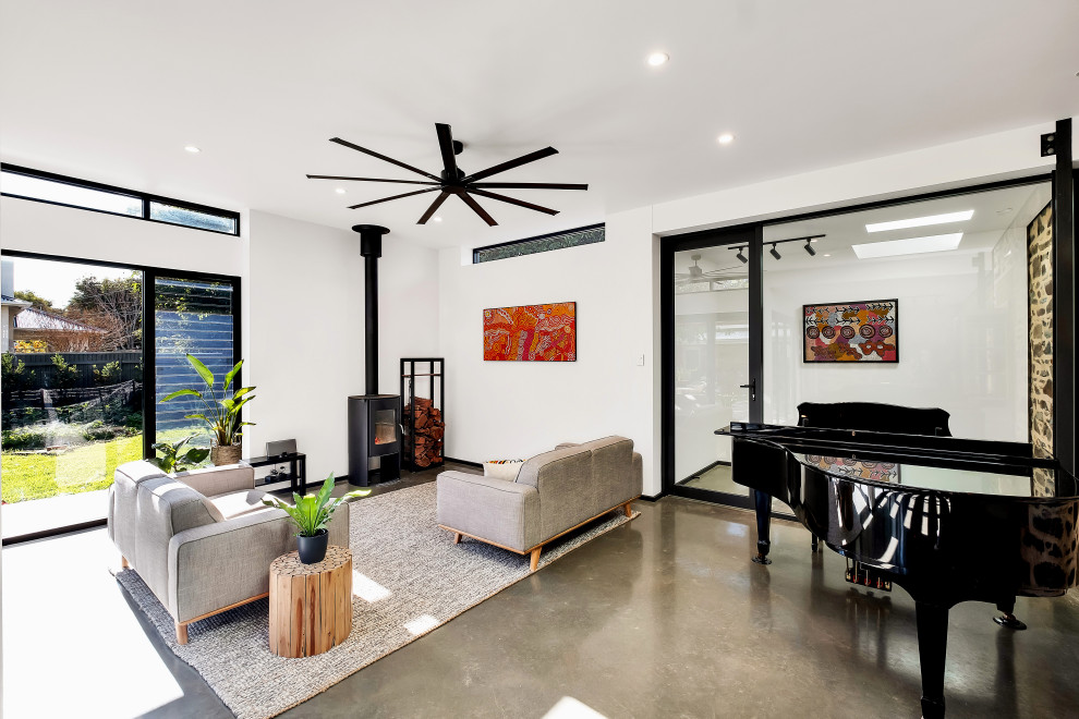 Large contemporary open concept living room in Adelaide with white walls, concrete floors, a wood stove, grey floor and a music area.