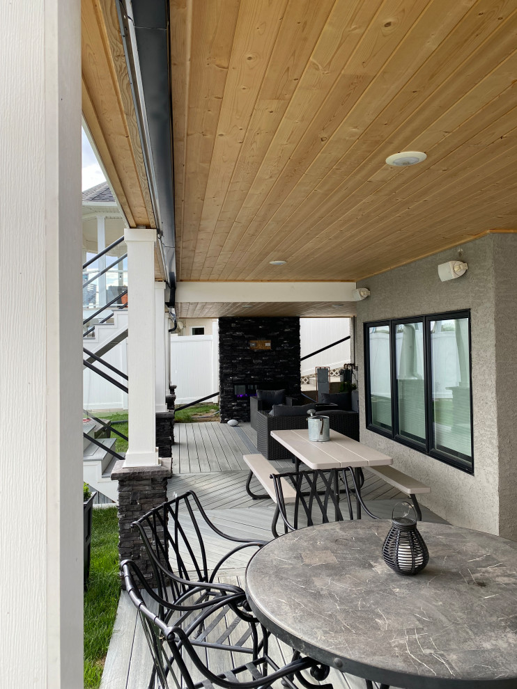 Example of a large minimalist backyard second story glass railing deck design with a fireplace and a roof extension