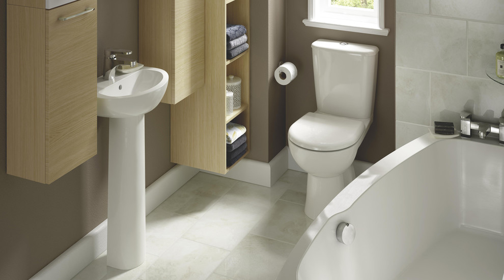 This is an example of a small contemporary bathroom in Hampshire with a wall-mount sink, furniture-like cabinets, light wood cabinets, a drop-in tub, a one-piece toilet, beige tile, brown walls and ceramic floors.