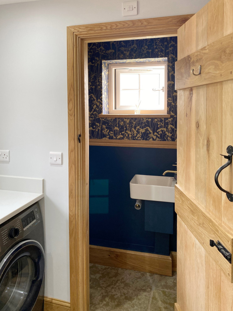 This is an example of a mid-sized contemporary galley dedicated laundry room in Other with a farmhouse sink, shaker cabinets, blue cabinets, marble benchtops, white splashback, marble splashback, white walls, limestone floors, a side-by-side washer and dryer, beige floor and white benchtop.