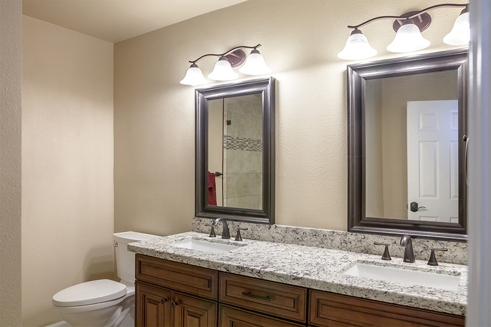 Alcove shower - mid-sized transitional master beige tile and porcelain tile porcelain tile and beige floor alcove shower idea in Phoenix with shaker cabinets, dark wood cabinets, a two-piece toilet, beige walls, an undermount sink, granite countertops and a hinged shower door