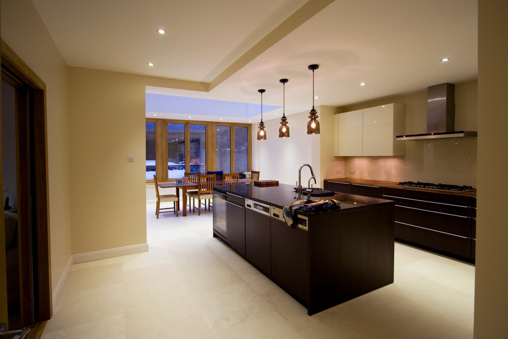 Photo of a large traditional galley eat-in kitchen in London with an integrated sink, shaker cabinets, dark wood cabinets, wood benchtops, beige splashback, glass sheet splashback, stainless steel appliances, porcelain floors and with island.