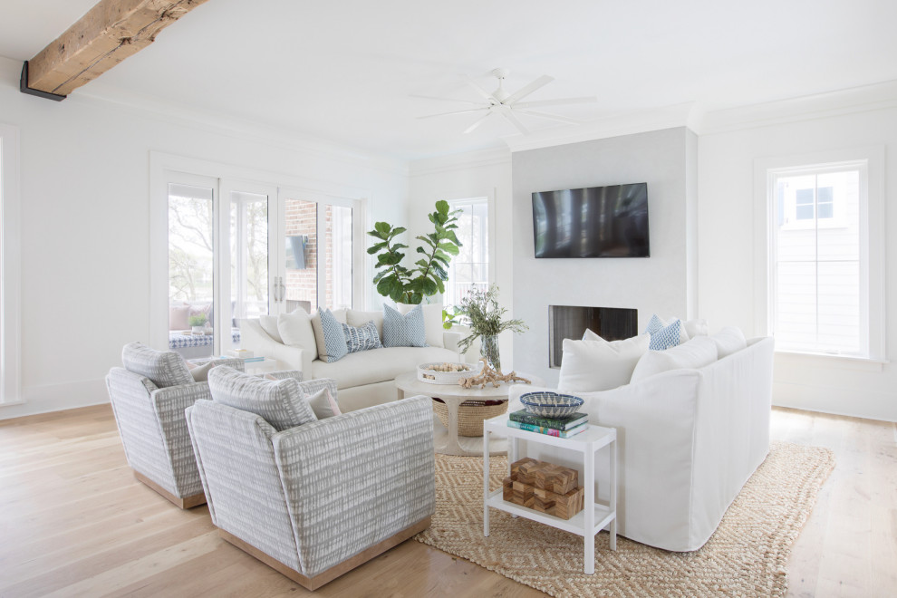 Design ideas for a beach style living room in Charleston with white walls, light hardwood floors, a standard fireplace and beige floor.