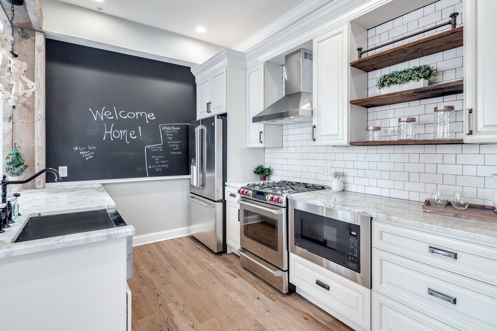 Mid-sized modern galley eat-in kitchen in Philadelphia with a farmhouse sink, raised-panel cabinets, beige cabinets, granite benchtops, white splashback, cement tile splashback, stainless steel appliances, light hardwood floors, no island and white benchtop.