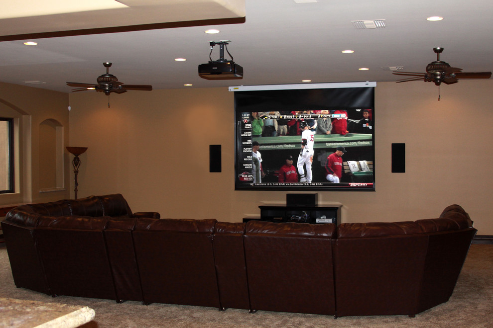 This is an example of a large open concept home theatre in Phoenix with a projector screen, beige walls and carpet.
