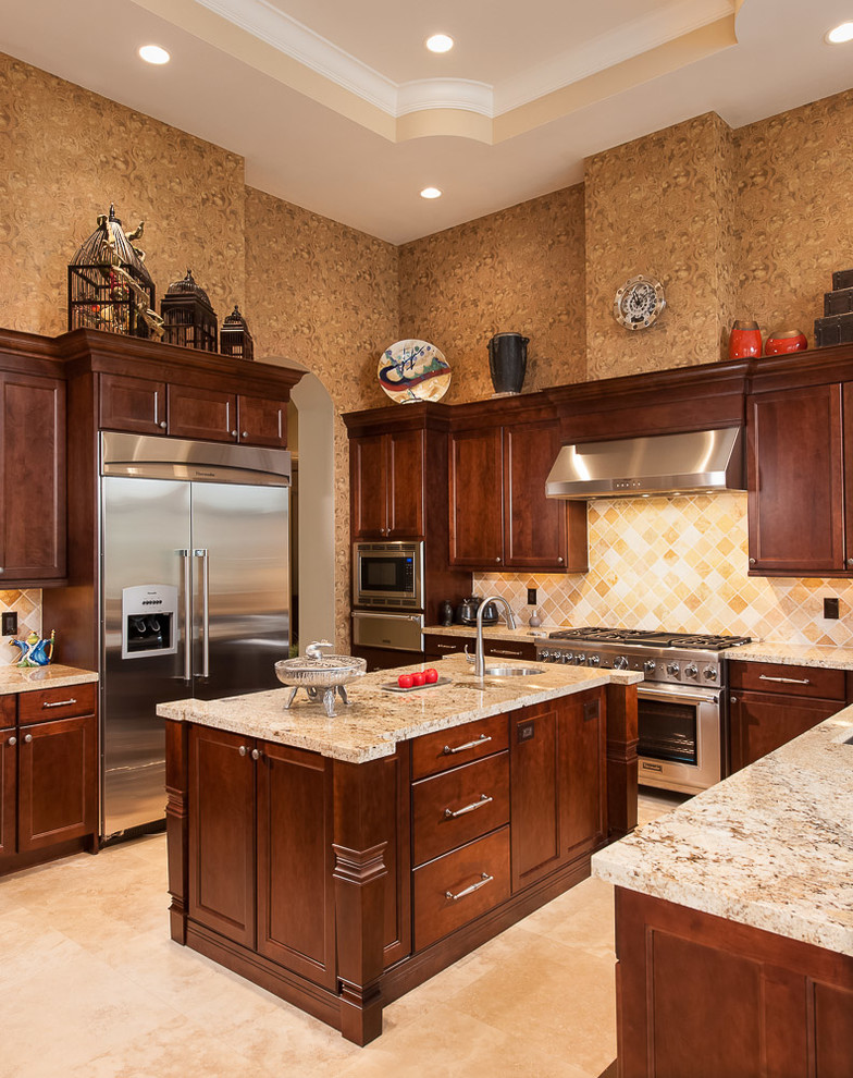 Photo of a large mediterranean u-shaped separate kitchen in Miami with recessed-panel cabinets, dark wood cabinets, granite benchtops, beige splashback, stainless steel appliances, a drop-in sink, stone tile splashback, travertine floors, with island and beige floor.